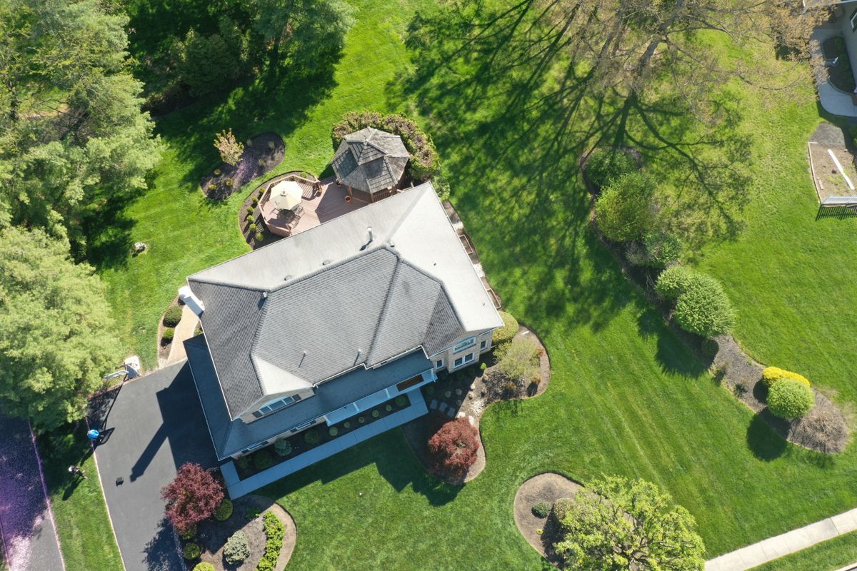 Drone view of a large colonial home in Blue Bell, PA with its old gray shingle roof
