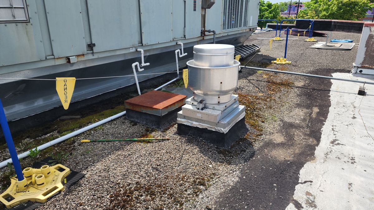 Worn gravel flat roof around a rooftop exhaust fan and HVAC unit before replacement