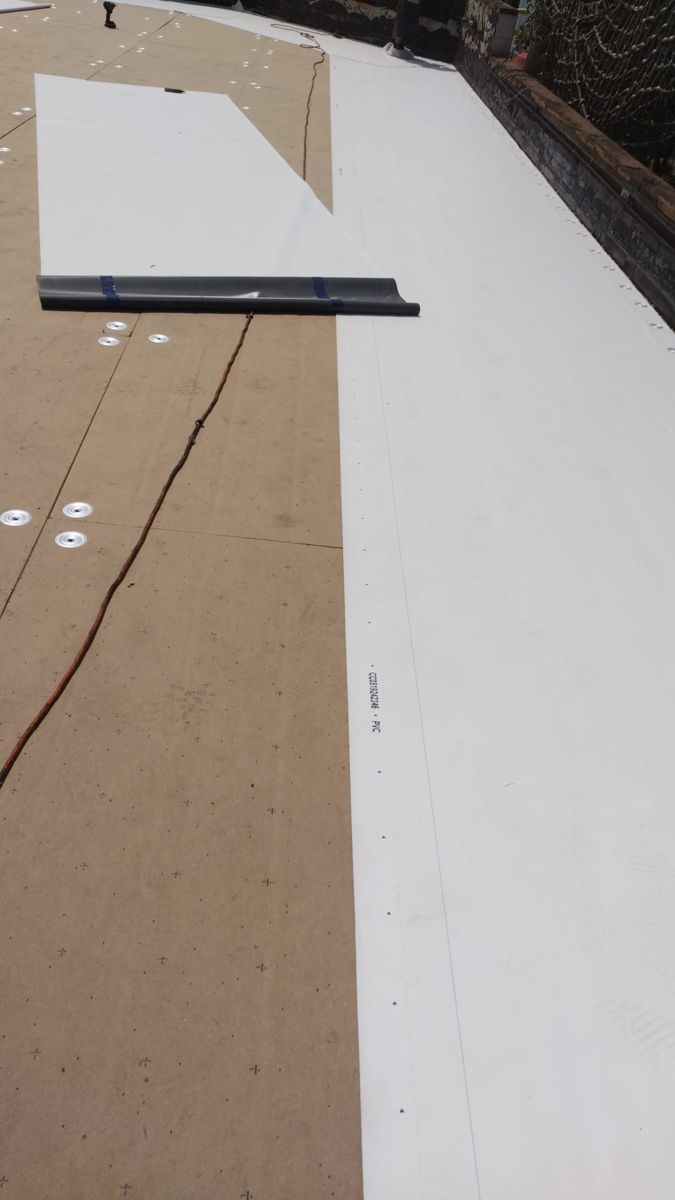 White single-ply membrane rolled out over new insulation board on a flat roof