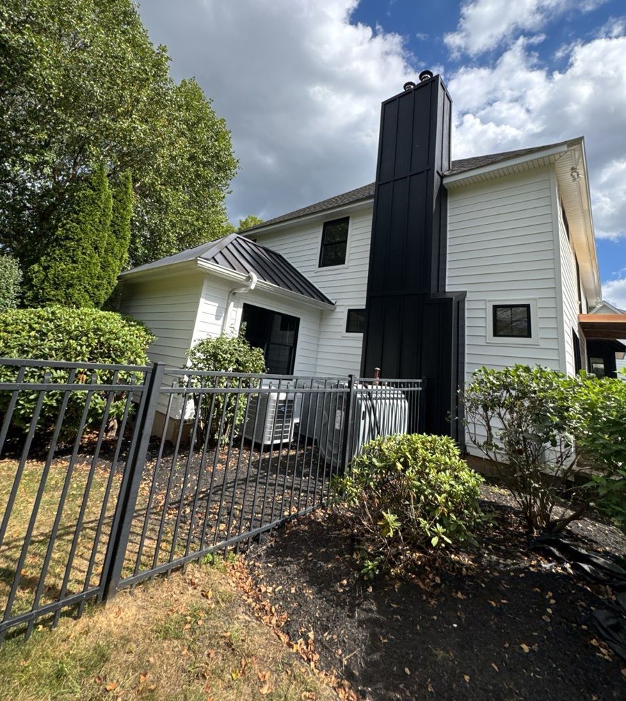 Chimney wrapped in black vertical board-and-batten siding next to white lap siding