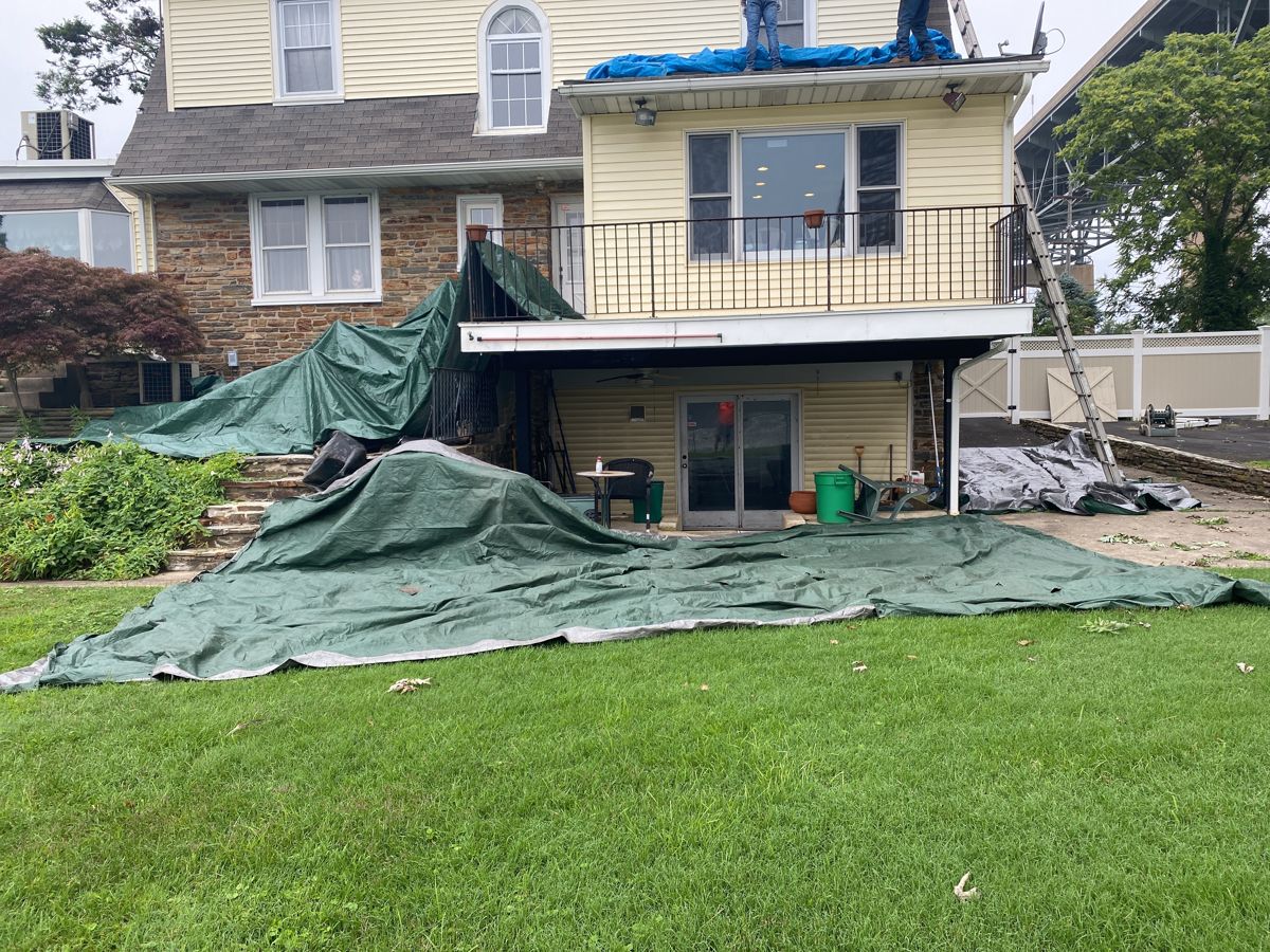 Tarps covering the lawn and roof during a roof replacement on a riverfront home in Bristol, PA