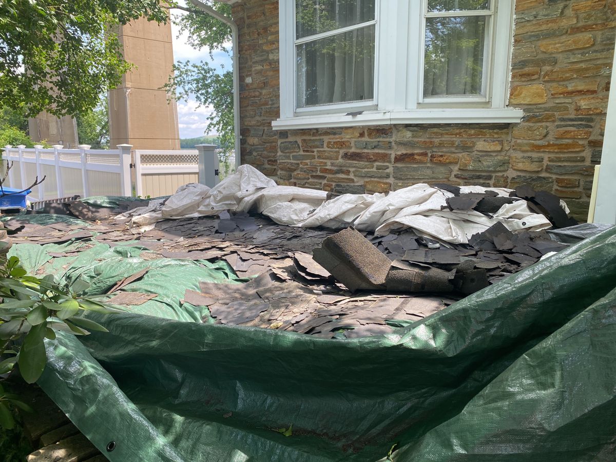 Old shingles torn off onto tarps beside a stone wall in Bristol, PA
