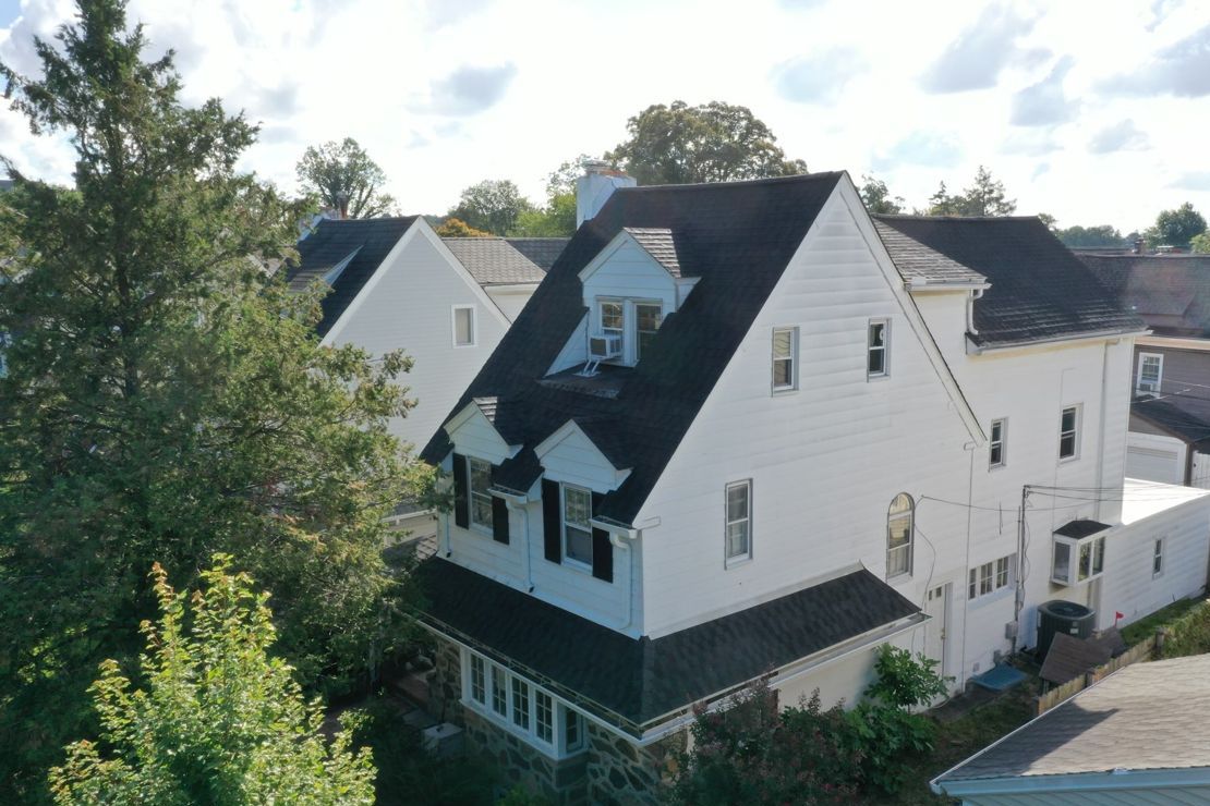 Drone view of a finished dark shingle roof on a white colonial with dormers in Penn Wynne, PA