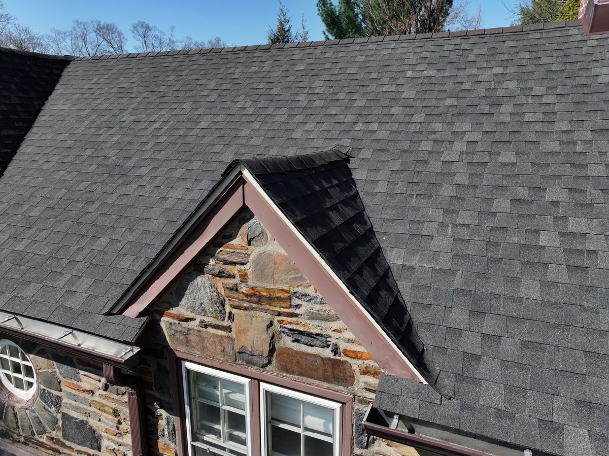 Drone view of a new dark GAF Timberline HDZ shingle roof over a stone gable in Merion Station, PA