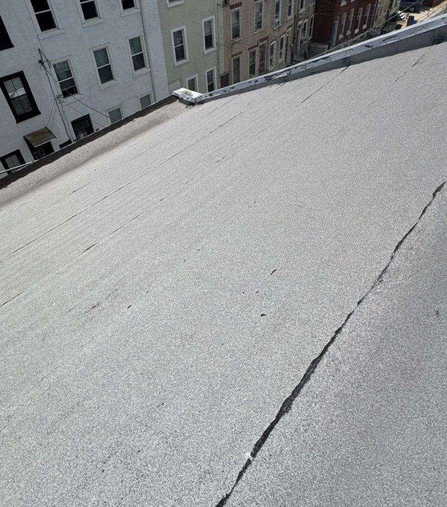 Cracked old flat roof on a Manayunk rowhome with the rowhomes across the street behind it