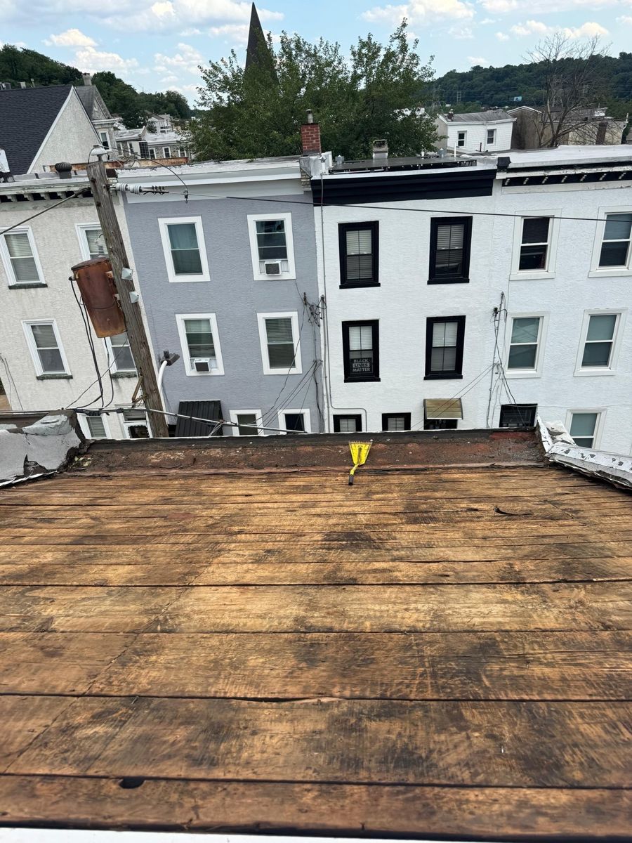 Original plank roof deck exposed after tear-off on a Manayunk rowhome, with rowhomes and a church steeple behind