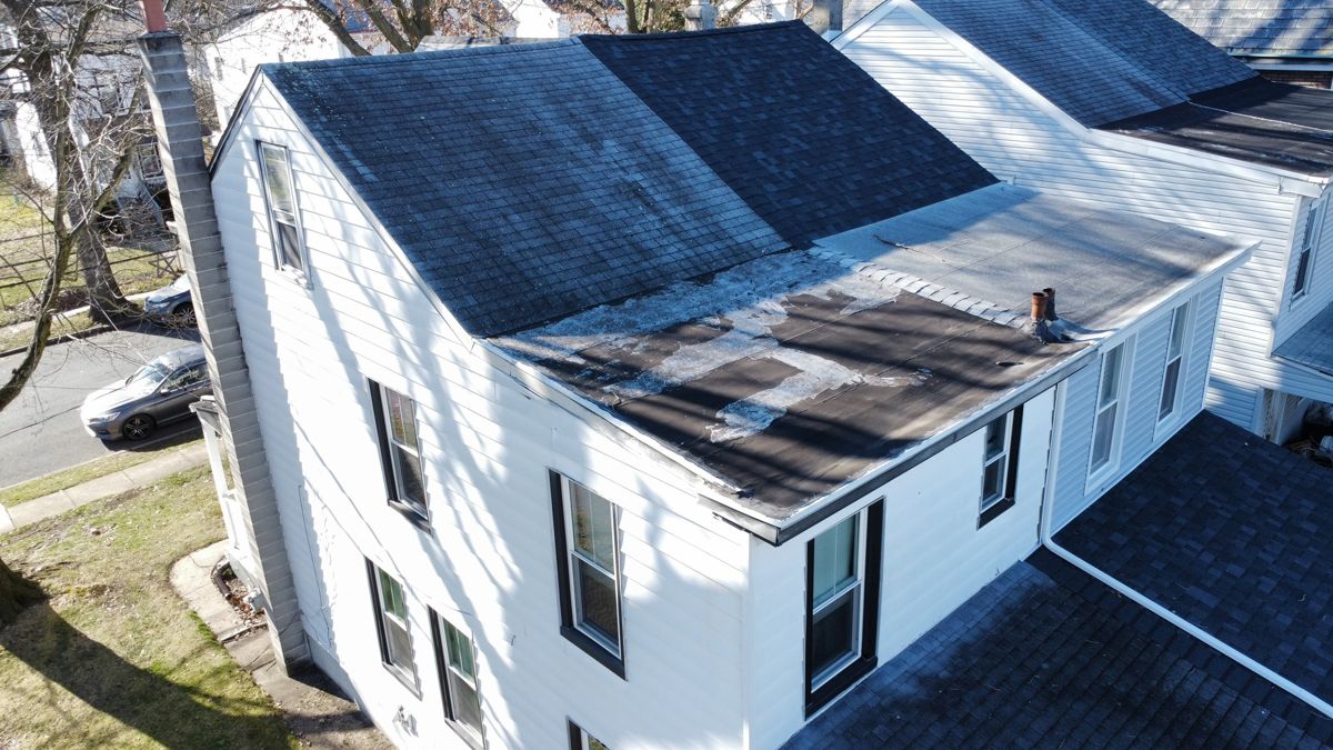 Aerial view of worn shingles and a patched low-slope rear roof on a Morrisville home