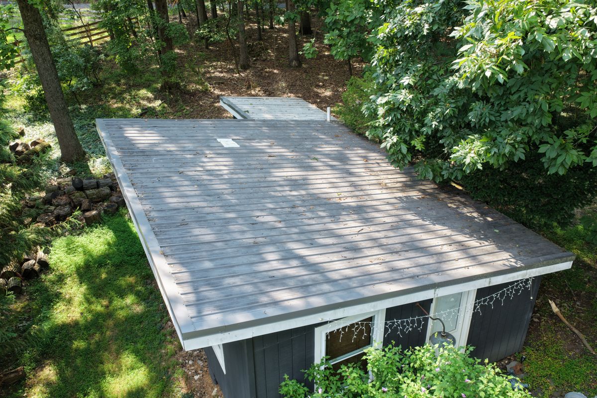 Weathered low-slope roof on a detached guest house on a wooded New Hope lot