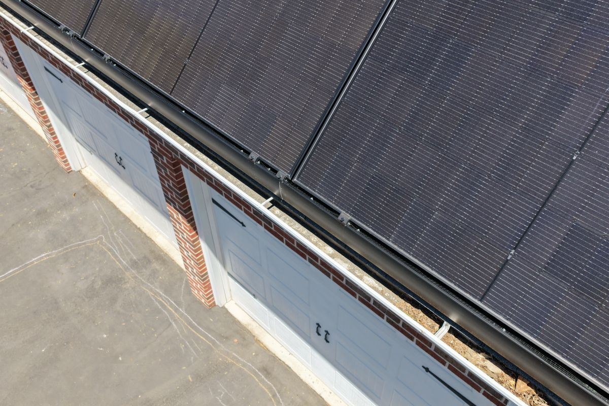 Old gutter packed with leaves and debris below solar panels on a Newtown garage roof