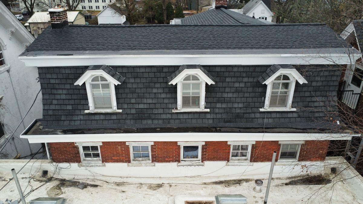 Older brick building with a re-roofed mansard, three arched dormers and white flat roofs in North Wales, PA