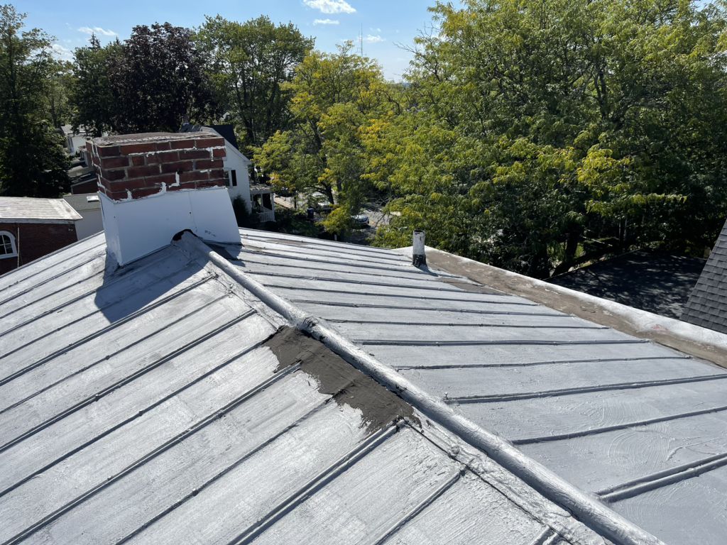 Old painted metal roof with patched seams on an older brick building in North Wales, PA