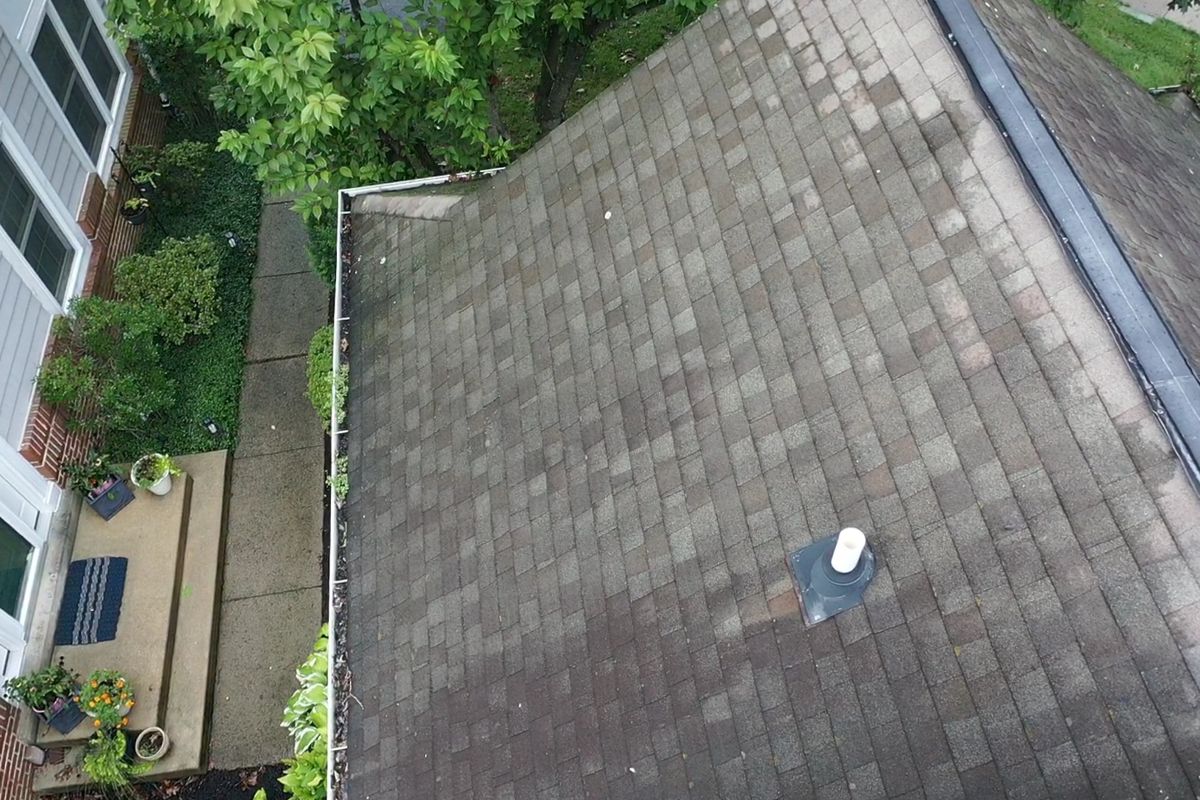 Stained, worn shingles and a gutter full of debris on a Yardley roof before replacement